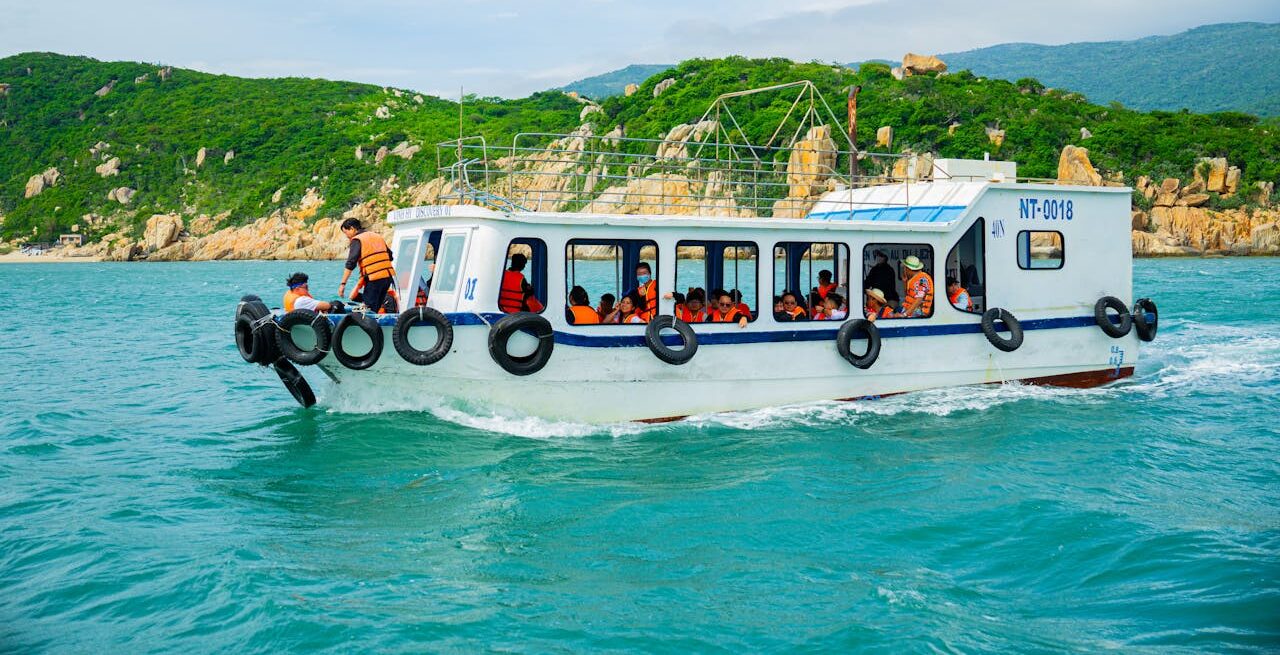 A boat filled with tourists in life jackets traverses vibrant turquoise waters along a lush, green coastline.