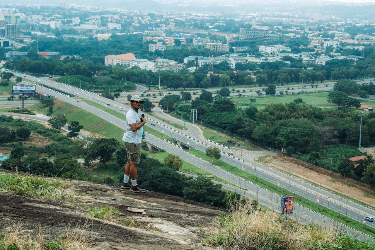 A hiker stands on a hill overlooking a sprawling cityscape under a cloudy sky.