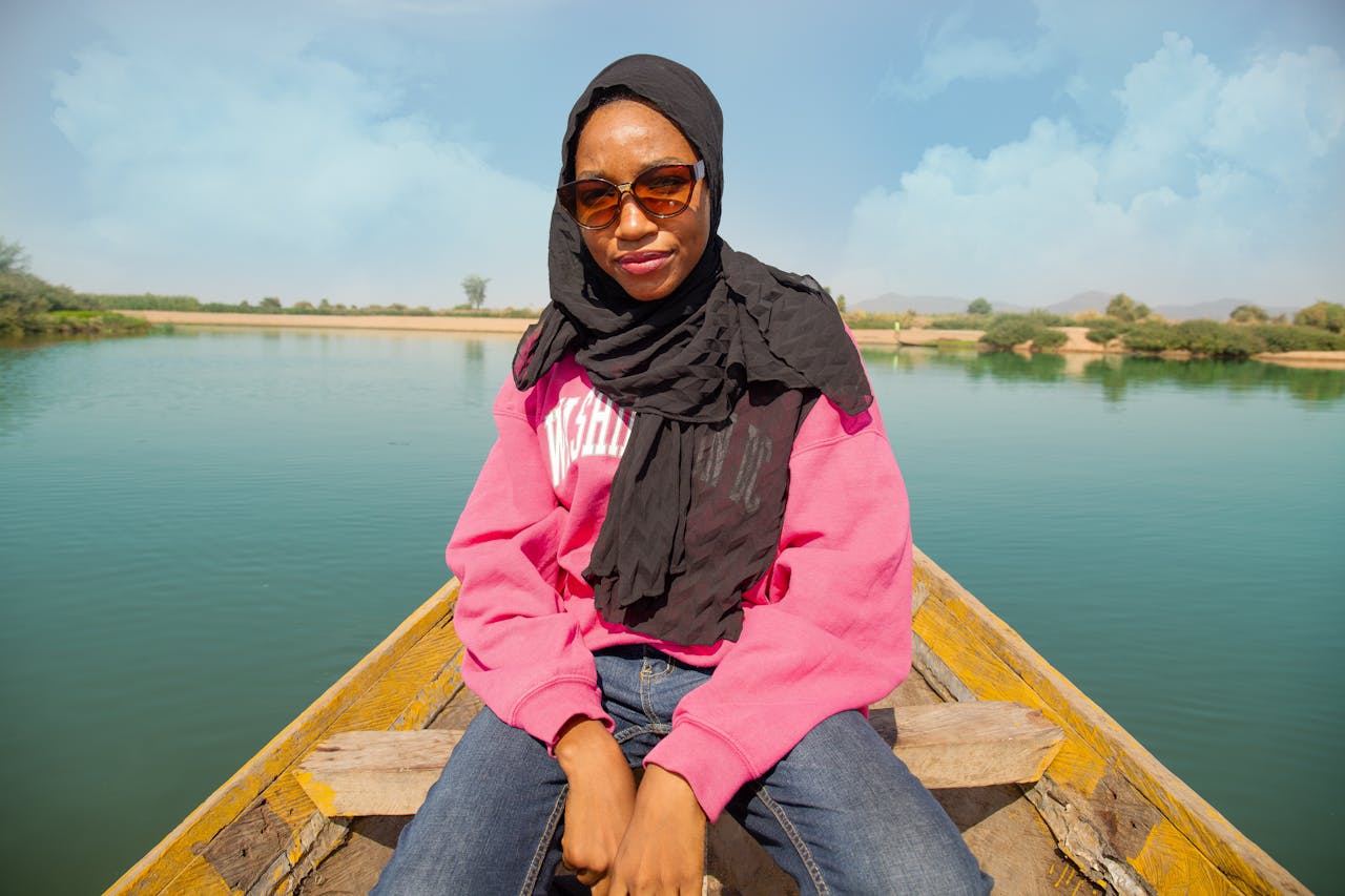 Portrait of a woman in a headscarf on a boat with a scenic lake background in Nigeria.